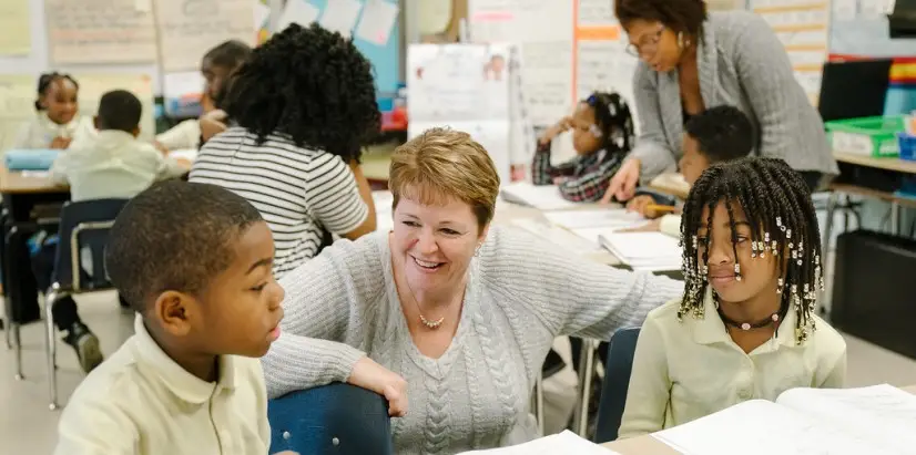 A teacher speaks to two students in a classroom.