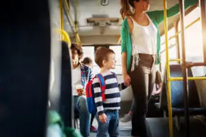 Young beautiful mother is holding her little toddlers hand while holding onto the bars with other hand and standing in the bus.