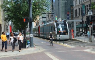 People crossing the street in Downtown Houston, while a cyclist and METROrail wait at the red light