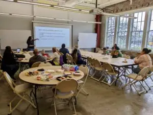 Mara Gomez presents on the I-45 expansion and explains the process to provide comments to the FHWA to a group of residents seated at tables at a community meeting.