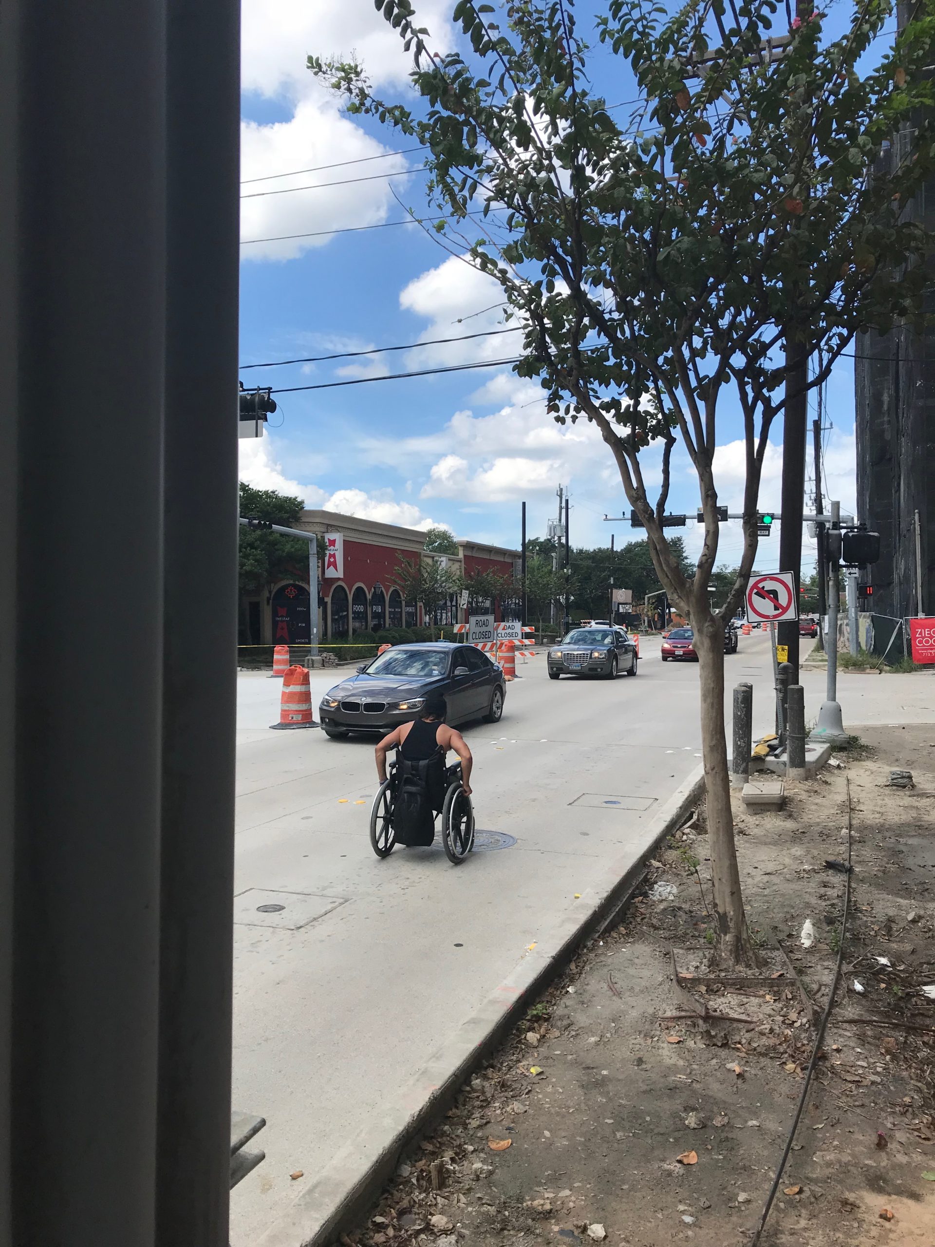 A man in a wheelchair rolling on the street because there is no sidewalk.